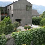 Viditelný jasný kontrast šedivého betonového fasádního systému a syté zeleně.